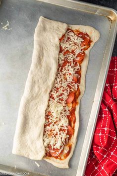 an uncooked pizza with cheese and sauce on it in a baking pan next to a red towel