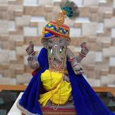 a statue of an elephant wearing a blue and yellow outfit is on a table in front of a brick wall