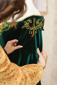 a woman in a green and gold dress is looking at something on the mannequin