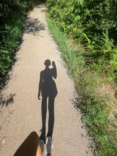 the shadow of a person standing on a dirt road next to bushes and trees,