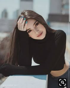 a woman with long brown hair and black shirt leaning on a wall looking at the camera