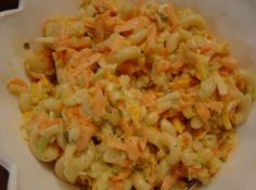 a white bowl filled with macaroni salad on top of a wooden table next to a fork