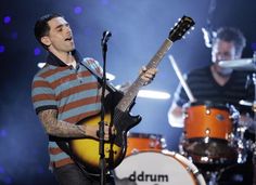 a man holding a guitar while standing next to another person on a stage with microphones