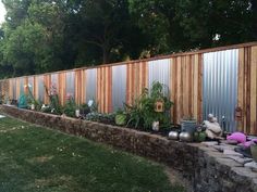 an outdoor garden area with various plants and flowers on the side of a fenced in yard