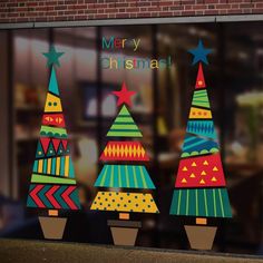 three brightly colored christmas trees in front of a store window