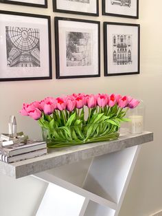 pink tulips in a glass vase on a table with books and pictures behind them