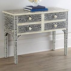 an ornate white and black dresser with flowers on it's side table next to a wall