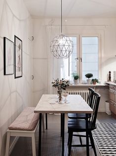 a kitchen table with two chairs and a bench in front of the window, next to a potted plant