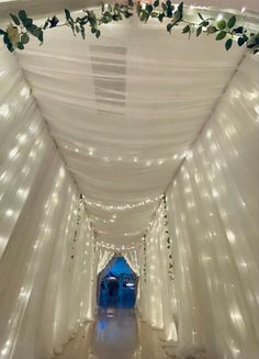 the inside of a white tent with lights and greenery on the ceiling is lit up