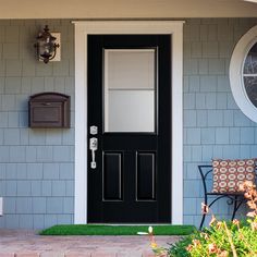 a black front door on a house with grass in the foreground and a chair outside