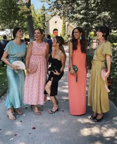 four women in dresses are standing together on the sidewalk and laughing at each other while one woman holds her purse