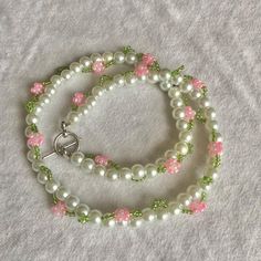 a white and green beaded bracelet with pink flowers on the clasp, sitting on a gray surface