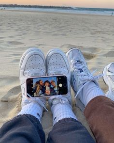 someone taking a selfie with their cell phone on the beach while wearing tennis shoes