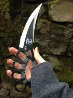 a person holding up a pair of scissors in their hand with moss growing on the rocks behind them