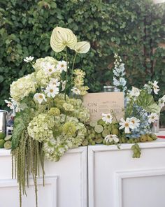 an arrangement of flowers and greenery on top of a cabinet