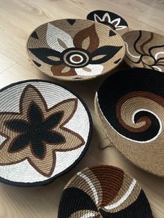 four woven baskets with designs on them sitting on a wooden floor next to each other