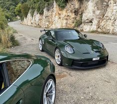 two green sports cars parked next to each other on the side of a mountain road