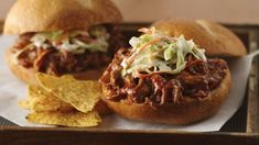 two pulled pork sandwiches with coleslaw and tortilla chips on a tray