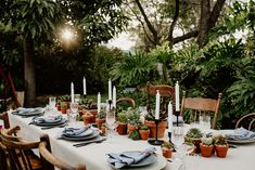 an outdoor table set for dinner with succulents, candles and place settings