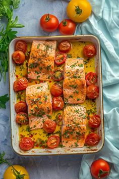 salmon and tomatoes in a baking dish on a blue tablecloth next to cherry tomatoes