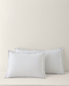 two pillows sitting on top of a bed next to each other in front of a white wall