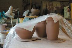 three clay vases sitting on top of a table covered in plastic sheeting and surrounded by other pottery