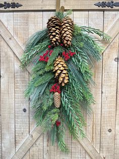 a pine cone wreath hanging on the side of a barn door with evergreen and red berries