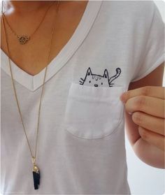 a person wearing a white shirt holding a gold necklace with a black cat on it