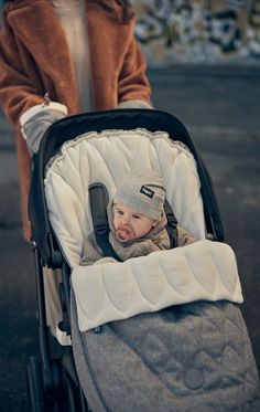 a woman pushing a stroller with a baby in it's seat and wearing a hat