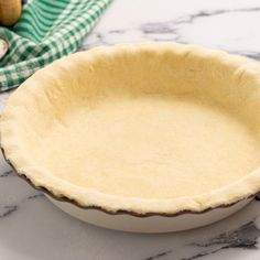 an uncooked pie crust in a bowl on a marble counter top with green and white checkered napkins