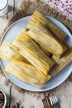 tamales on a white plate with silverware next to some nuts and a glass of milk