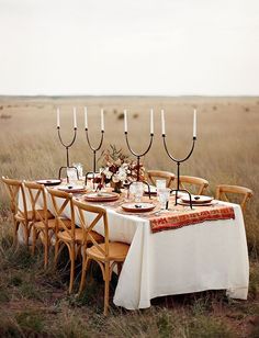 a table set with candles and plates in the middle of a field