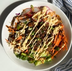 a white bowl filled with lots of food on top of a blue and white table cloth