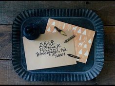 two pieces of paper with writing on them sitting on top of a blue tray next to a fountain pen