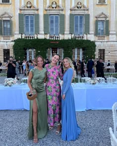 three women standing next to each other in front of a building