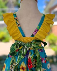 a dress with yellow ruffles and blue flowers on it, sitting on a mannequin