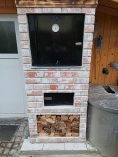 a brick fire place with logs stacked in front of it and a metal trash can next to it