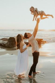 a man and woman holding up a baby on the beach