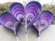 purple paper flowers are arranged on top of each other, with sticks sticking out of them