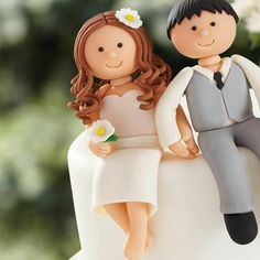 a bride and groom figurine sitting on top of a wedding cake with flowers in their hair