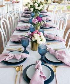 the table is set with blue and white plates, silverware, and pink napkins