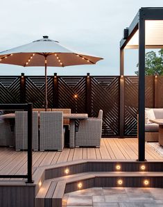 an outdoor deck with patio furniture and umbrellas lit up by lights on the sides