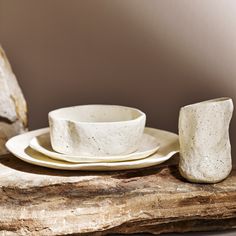 a white plate and bowl sitting on top of a piece of drift wood next to a cup