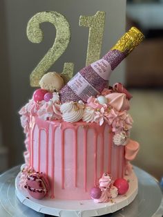 a pink and gold 21st birthday cake on a plate with a champagne bottle in the middle