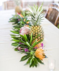 pineapples and other tropical flowers are lined up on a long white tablecloth