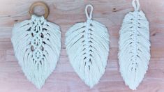 three white macrame leaf ornaments hanging on a wooden surface with a hook in the middle