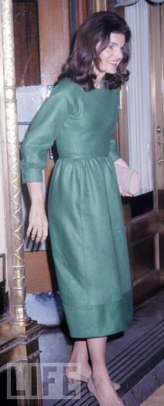 a woman in a green dress is walking down the stairs with her hand on her hip