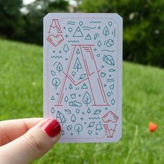 a hand holding up a card with the letter a on it in front of some green grass