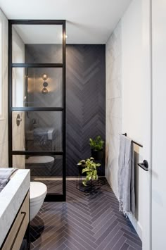 a bathroom with black and white herringbone tile on the floor, shower stall, toilet and sink