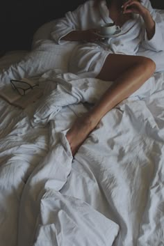 a woman laying in bed drinking from a cup